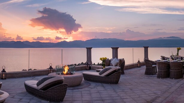 A terrace with wicker furniture, a fire feature, and a view of the sea and mountains. - Hilton Yuxi Fuxian Lake (Yuxi)