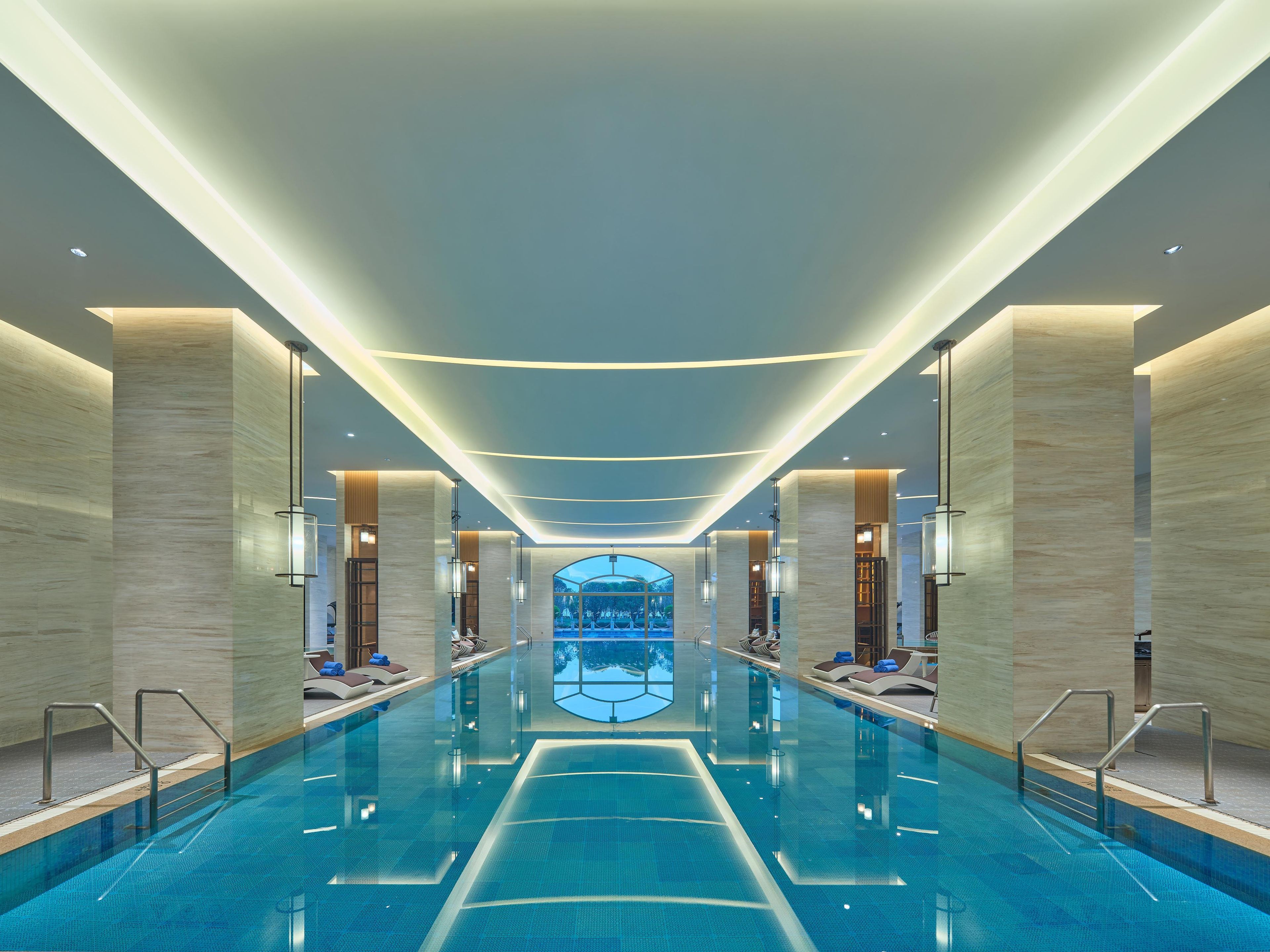 A modern indoor swimming pool with clear water, surrounded by high ceilings and contemporary lighting fixtures.