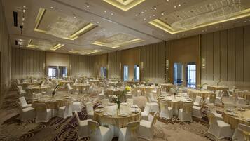 A large banquet hall with round tables, white chairs, and chandeliers.