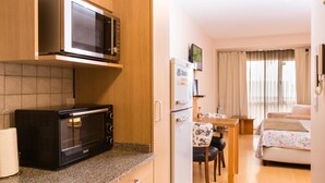 A compact kitchen with a microwave, toaster, and refrigerator. There is a dining area with a table and chairs, and a bed in the adjacent room. - San Martin Suites (San Carlos de Bariloche)