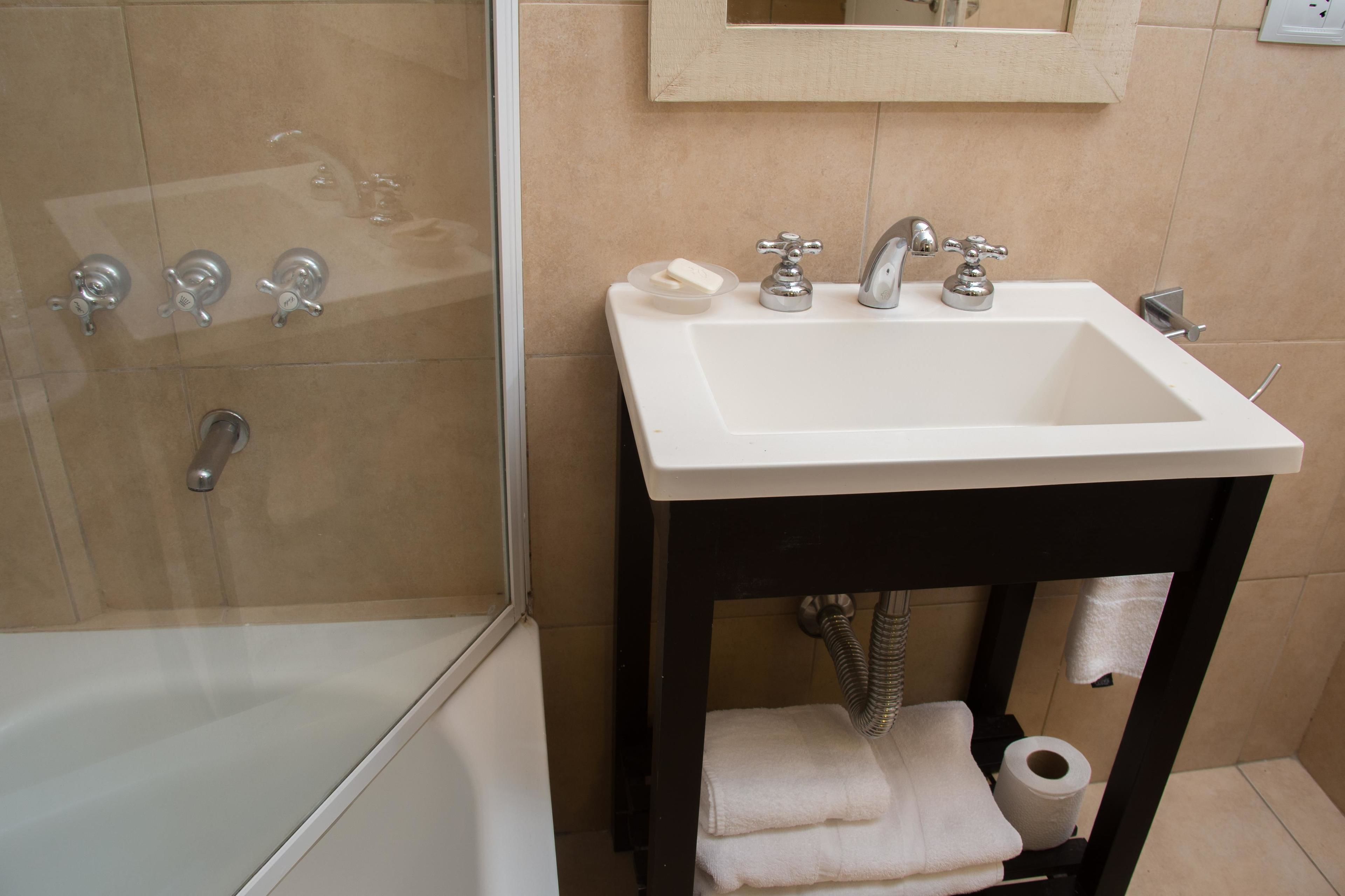 A bathroom with a white sink, two faucets, a mirror, a towel rack, and a shower area.