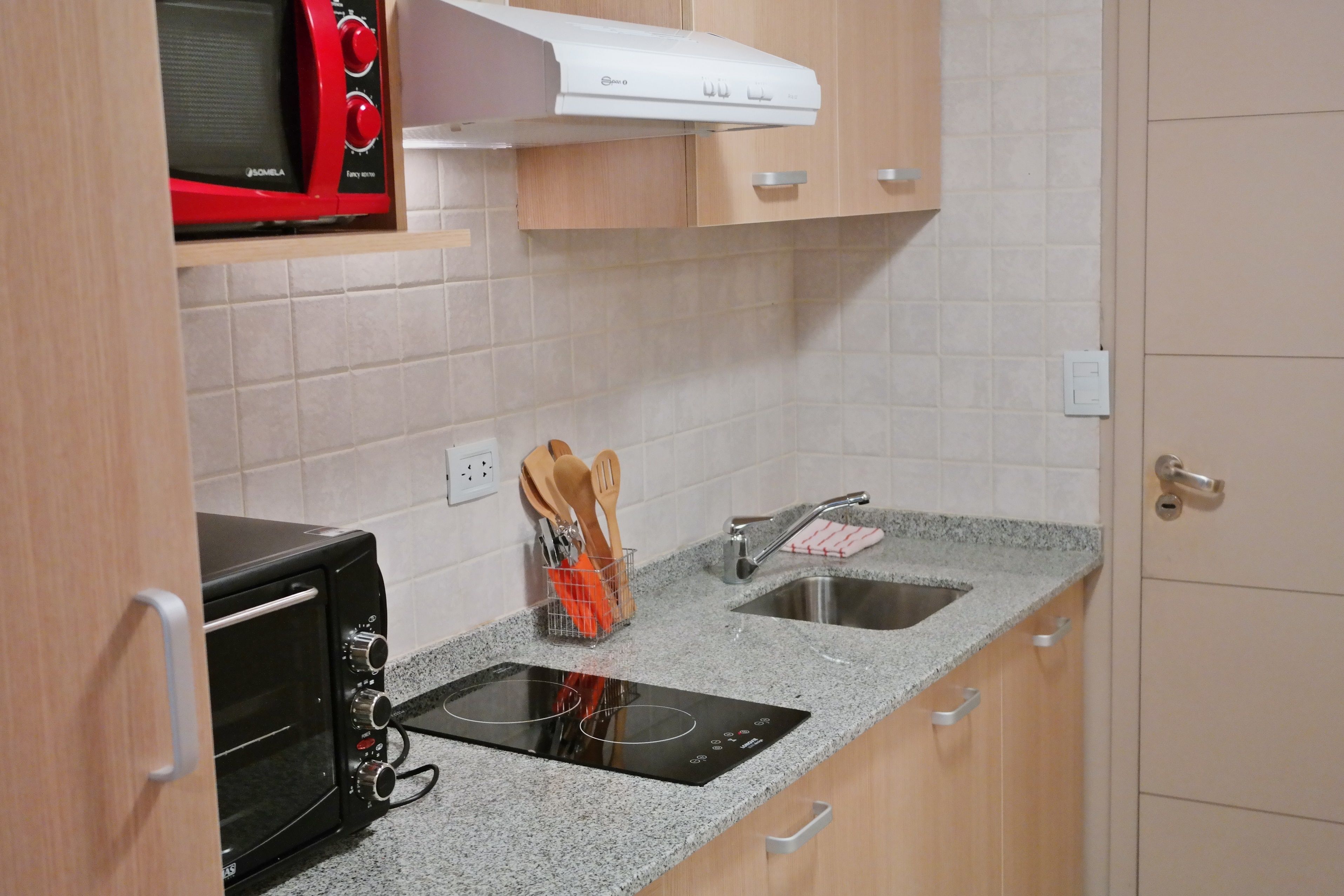Une cuisine compacte équipée d’un four à micro-ondes, d’un grille-pain, d’une plaque de cuisson à induction et d’un évier.