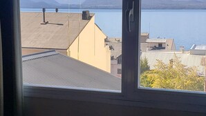 A view through a window of a building with a mountain backdrop and a body of water. - San Martin Suites (San Carlos de Bariloche)