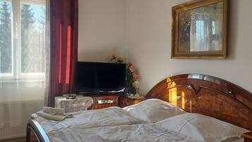 Une chambre à coucher comprenant un lit, une télévision, une table de chevet, un tableau encadré et une fenêtre avec des rideaux.