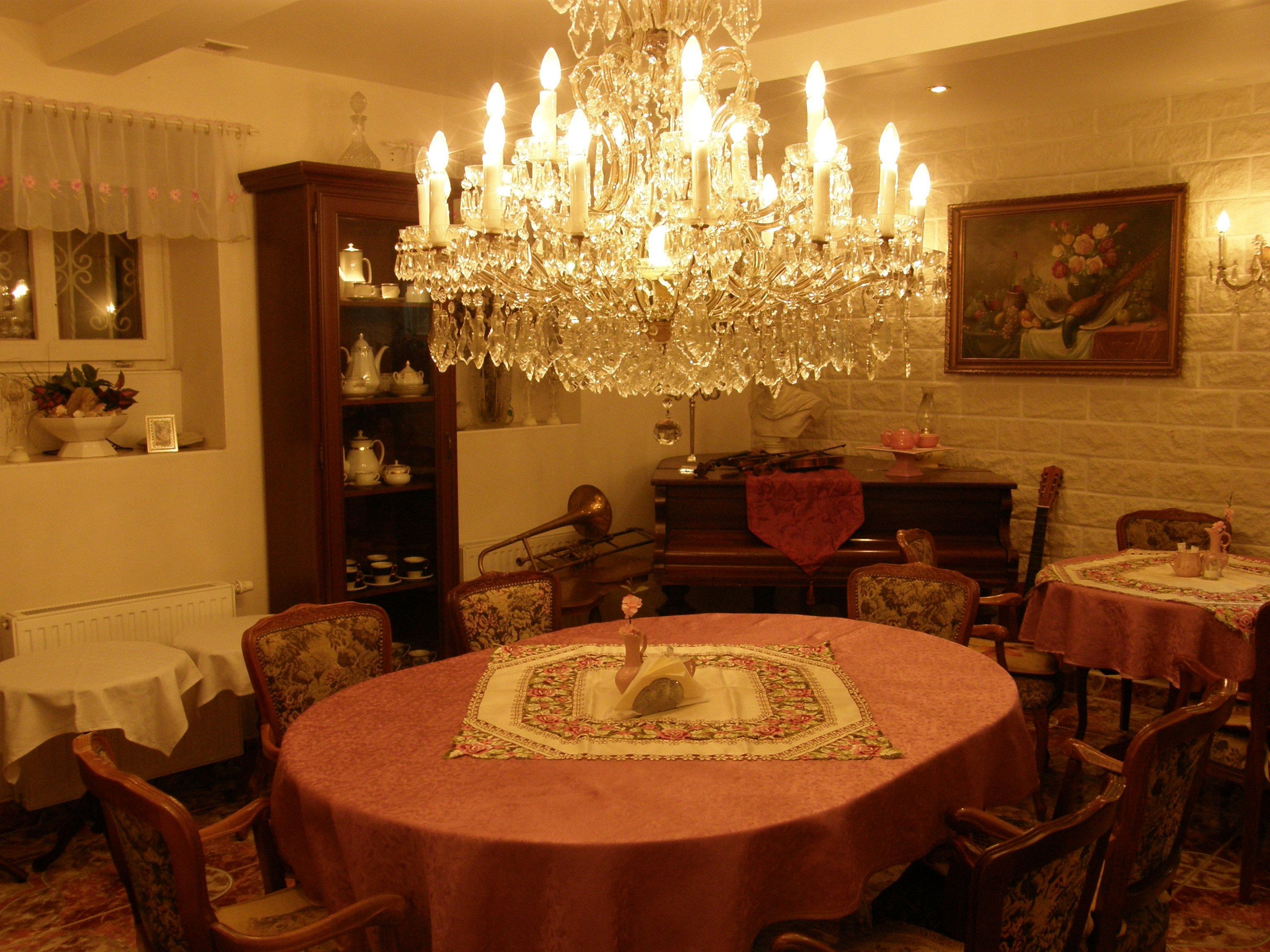 A dining area with a large chandelier, round tables with floral tablecloths, and a piano.