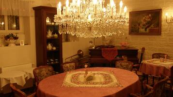 A dining area with a large chandelier, round tables with floral tablecloths, and a piano.