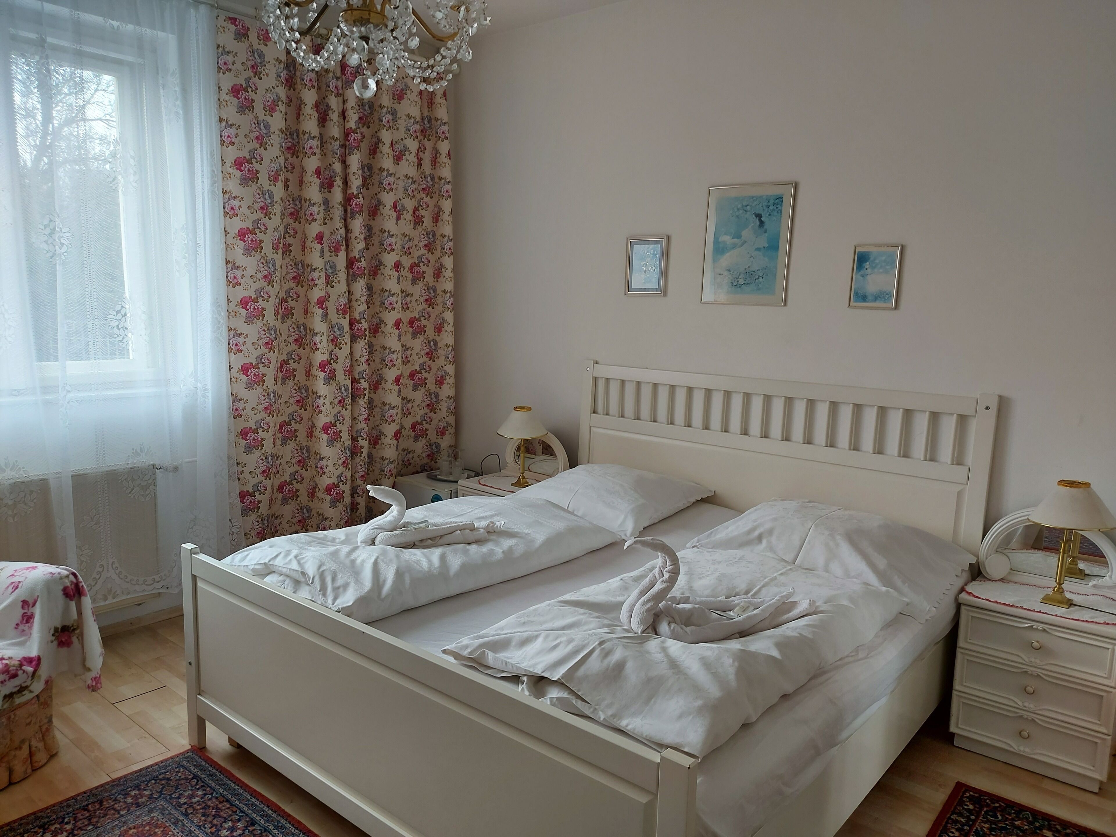 A bedroom with a bed, a nightstand, a lamp, a chair, and a window with curtains.