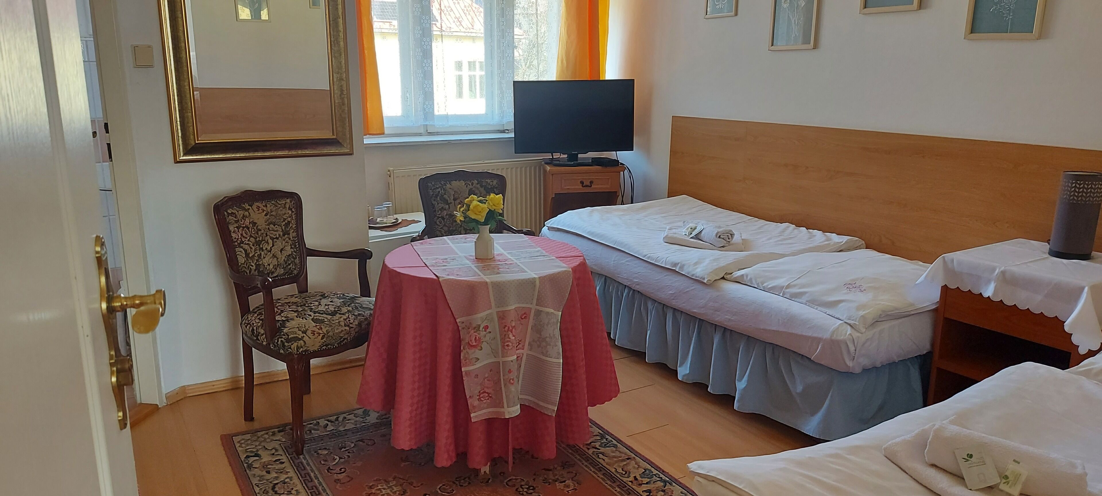 Habitación de hotel con cama, escritorio con televisor, silla, mesa con un florero y ventana con cortinas.