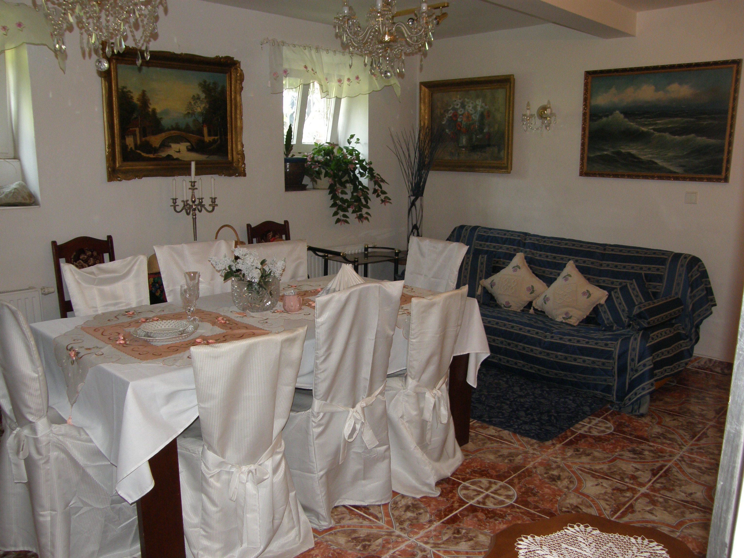 Un comedor con una mesa dispuesta para comer, sillas, un florero con flores y un sofá al fondo.
