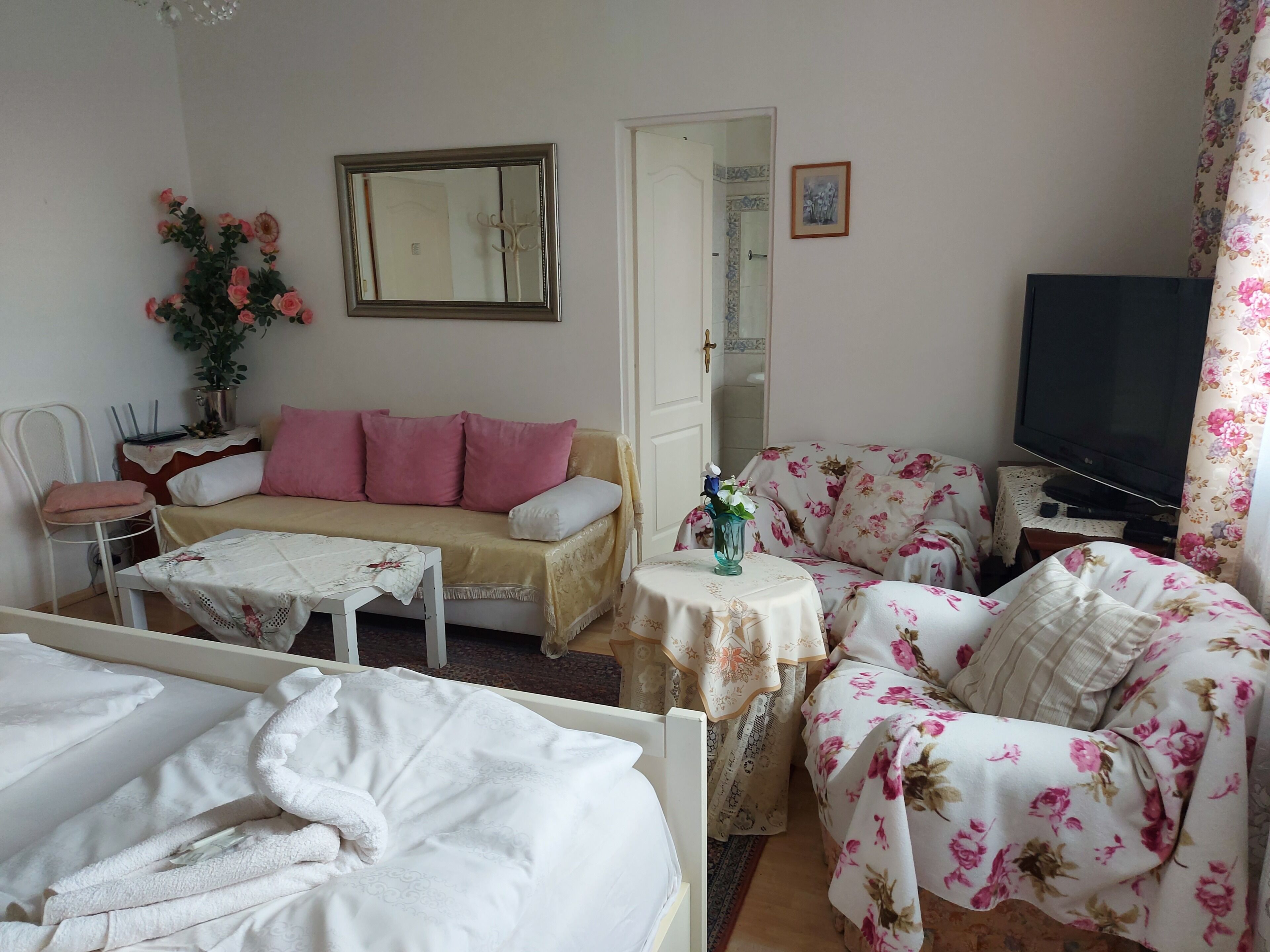 Una habitación con sofá, cama, televisor y una mesita con un florero.