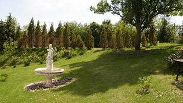 Ein Garten mit einer zentralen Fontäne, umgeben von ordentlich geschnittenen Hecken und verschiedenen Bäumen.