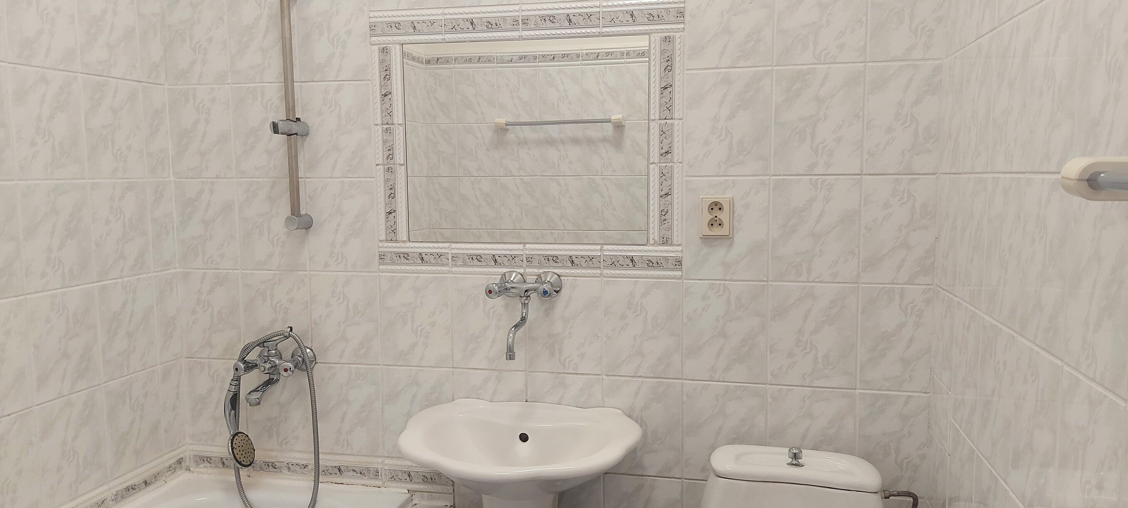 Baño con ducha, lavamanos e inodoro, todo con azulejos de mármol.