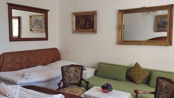 A room with a bed, a green sofa, a wooden chair, a table with a bowl, and three mirrors on the wall.
