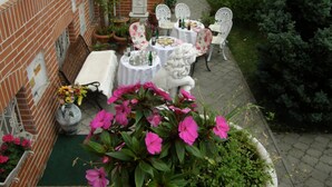 A patio with a brick wall, white outdoor furniture, and potted plants. - Hotel Garni (Ostrava)