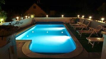 A rectangular swimming pool with a light blue interior, surrounded by a low wall and a deck area with lounge chairs.