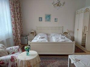A bedroom with a bed, two bedside tables, a chandelier, a mirror, and a floral-patterned chair. - Hotel Garni (Ostrava)