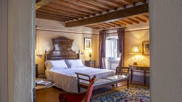 A bedroom with a large bed, a wooden ceiling, a red chair, and a patterned rug.