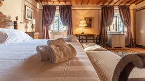 Une chambre d’hôtel avec un grand lit, une tête de lit en bois, un bureau avec une lampe et une vue sur l’extérieur par les fenêtres.
