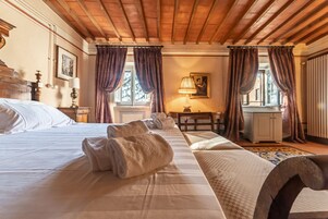 A hotel room with a large bed, a wooden headboard, a desk with a lamp, and a view of the outdoors through the windows.