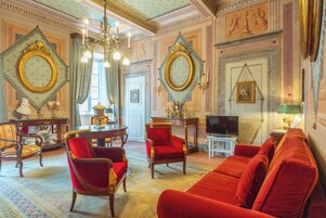 A luxurious room with ornate decorations, including a chandelier, red upholstered furniture, and a television.