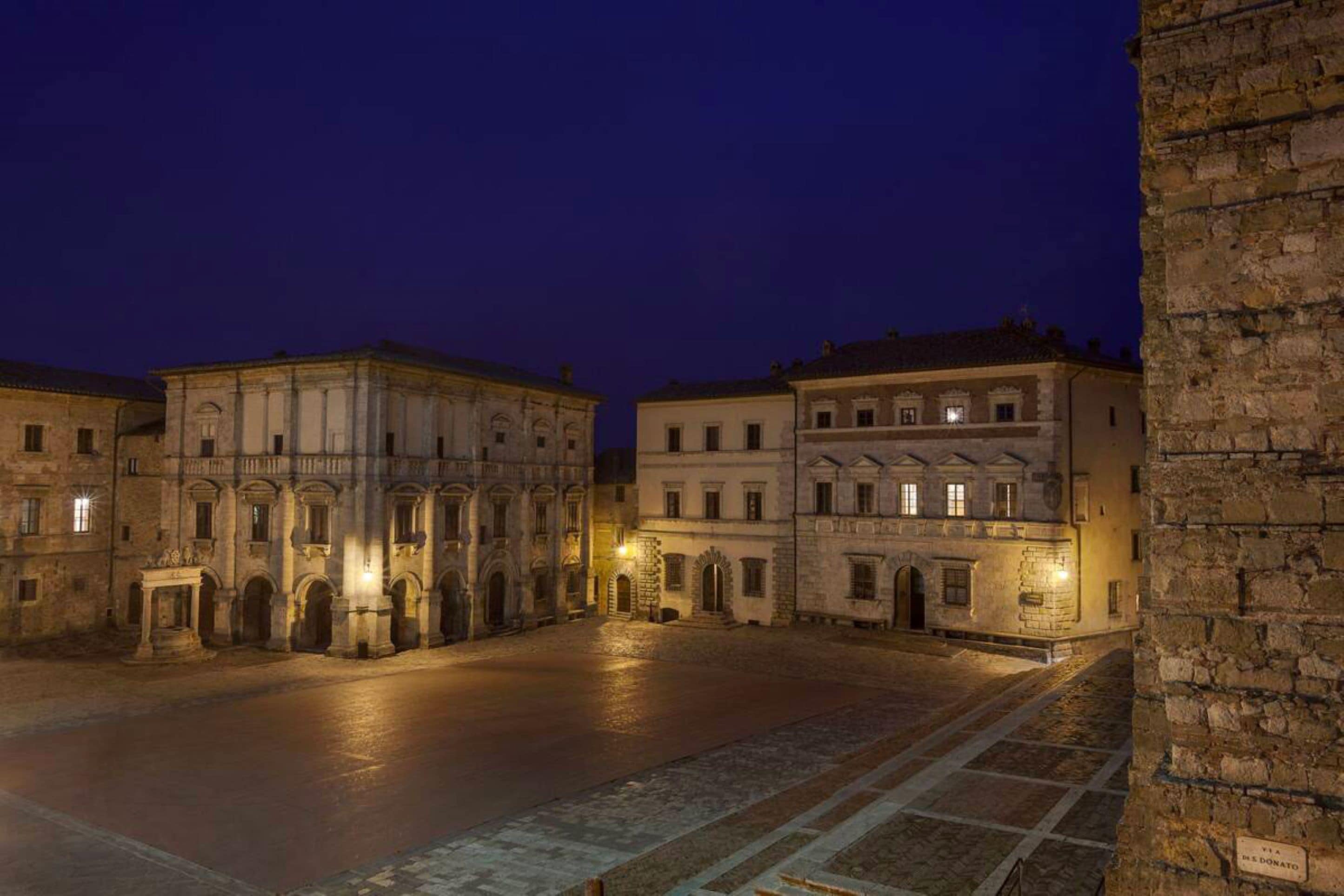 A historic square with buildings featuring classical architecture, a paved courtyard, and stone walls.