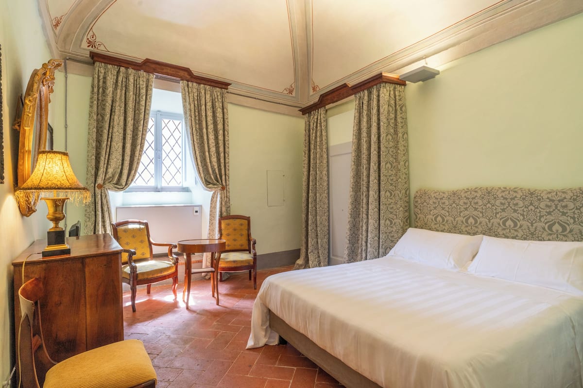 A hotel room with a bed, two chairs, a desk, and a lamp.