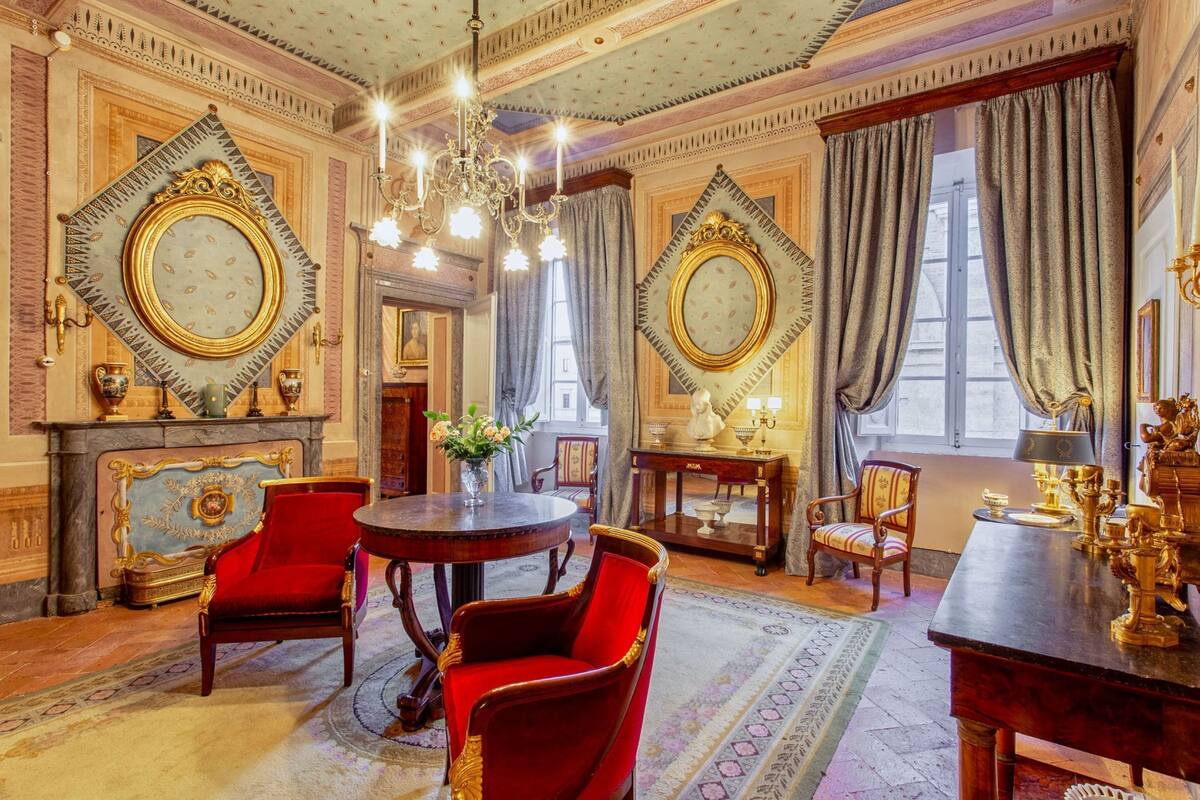 A grand room with ornate decorations, including a chandelier, red velvet chairs, and a large mirror.
