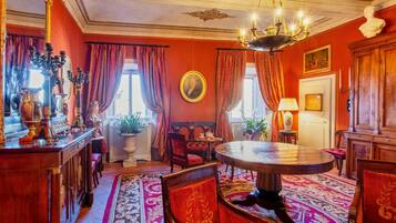 Quarto com uma mesa redonda de madeira, cadeiras estofadas em vermelho, um candelabro e um espelho grande.