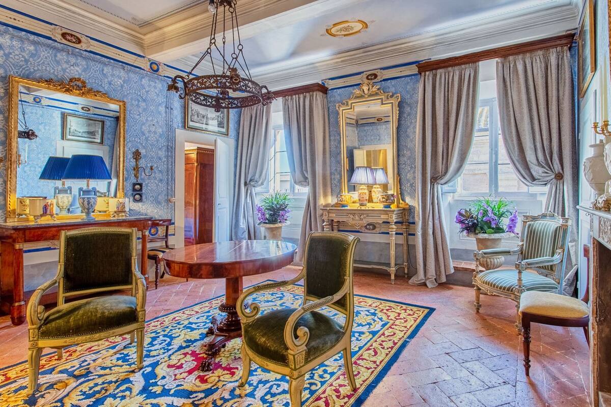 A room with a round wooden table, two chairs, a mirror, and a chandelier.