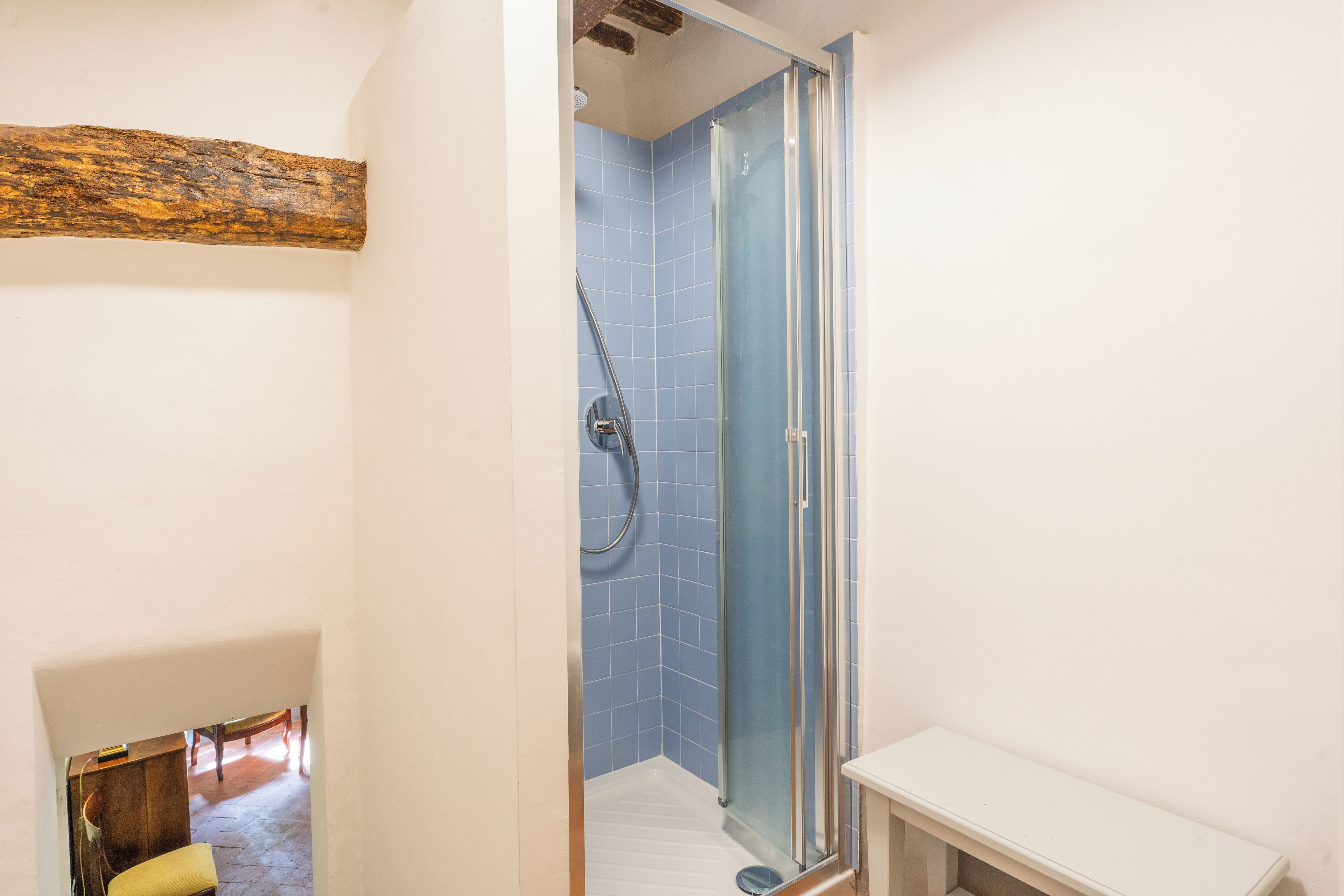 Ein Badezimmer mit Duschkabine aus Glas, weißen Wänden und einem Holzbalken über der Dusche.