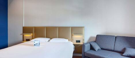 A hotel room with a large bed, a sofa, a small table, and a nightstand with lamps.