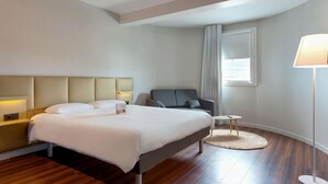 A hotel room with a bed, a chair, a small table, a lamp, and a window with curtains. - Ibis Budget La Roche sur Yon (Mouilleron-le-Captif)