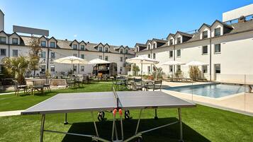 A courtyard with a ping pong table, outdoor seating, and a pool.