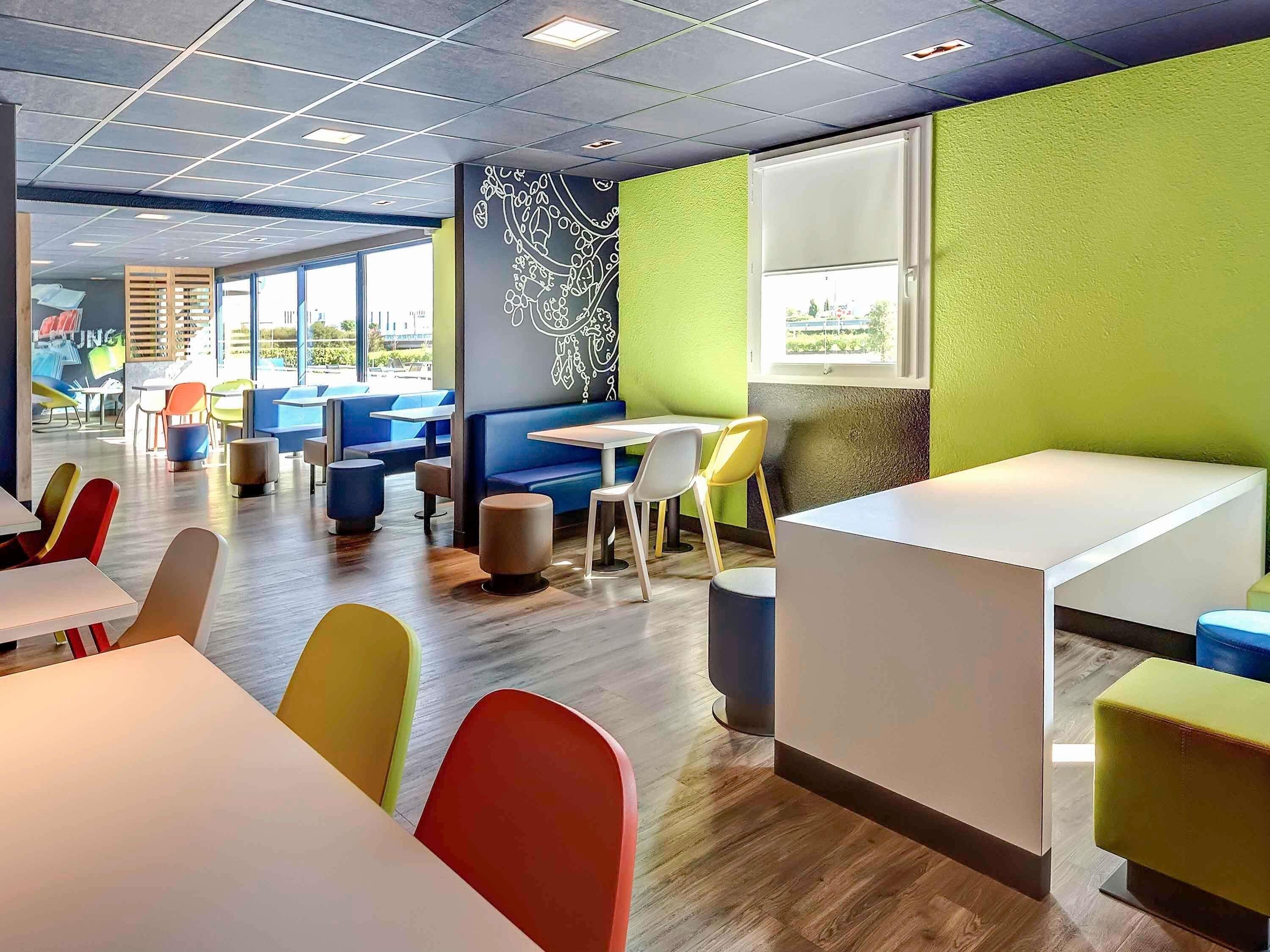 Un espace repas moderne avec des banquettes et des tables, de grandes fenêtres et un mur d’accent de couleur verte.