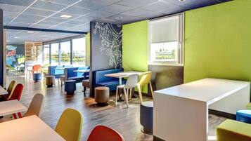 A modern dining area with booths and tables, large windows, and a green accent wall.