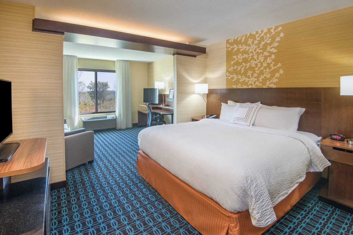 A hotel room with a large bed, a desk with a chair, a television, and a window with curtains.