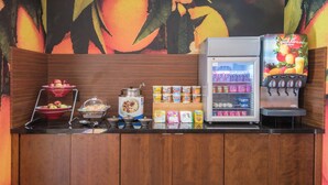 A breakfast bar with a fruit bowl, cereal boxes, a coffee machine, and a refrigerator. - Fairfield Inn & Suites Fort Wayne Southwest (Fort Wayne)