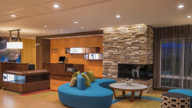 A modern lobby with a blue sofa, a round table, and a stone fireplace. - Fairfield Inn & Suites Fort Wayne Southwest (Fort Wayne)