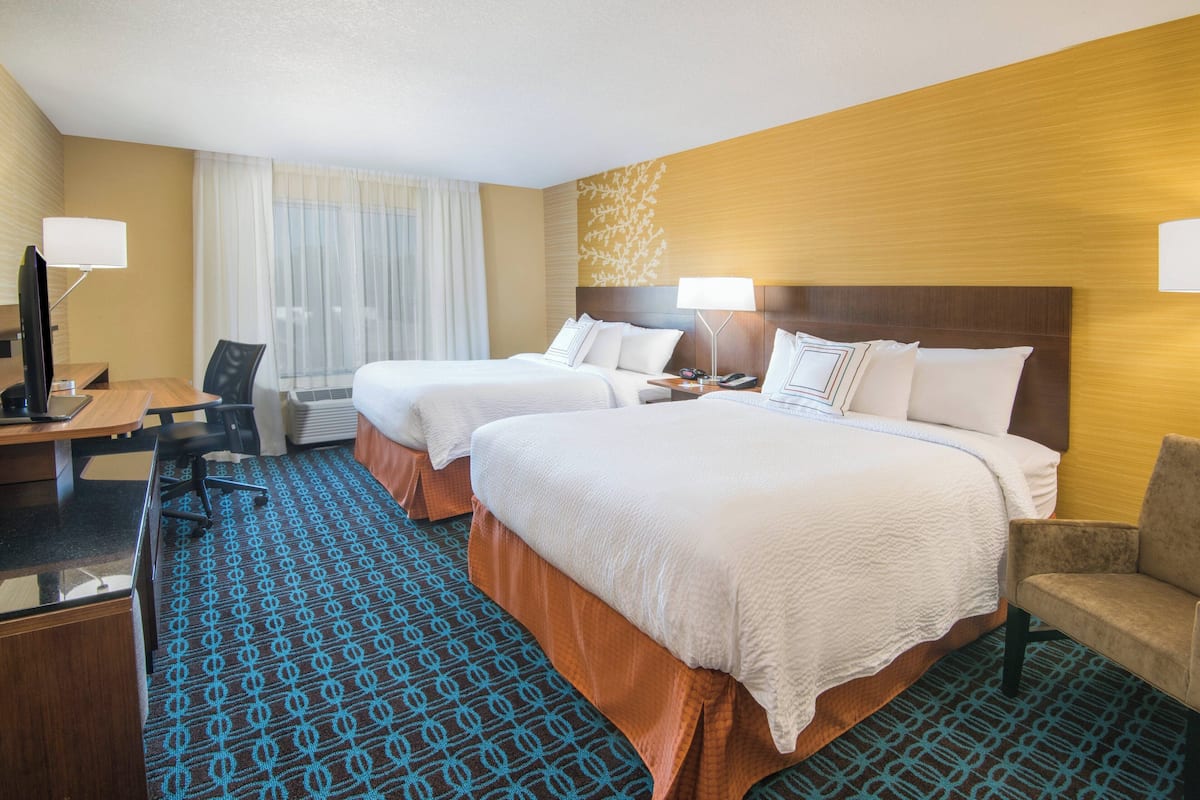 A hotel room with two beds, a desk, a chair, and a TV.