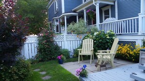A residential deck with two Adirondack chairs, a small table, and a potted plant. - The Colonel's In B&B (Fredericton)