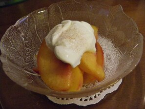 A glass bowl with a white doily underneath, containing sliced peaches and a dollop of whipped cream.