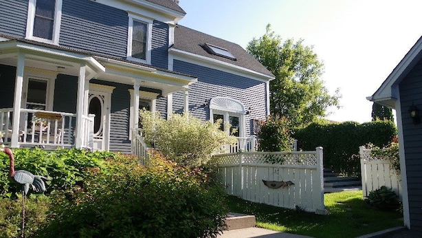 A two-story house with a porch, a picket fence, and a well-maintained lawn. - The Colonel's In B&B (Fredericton)