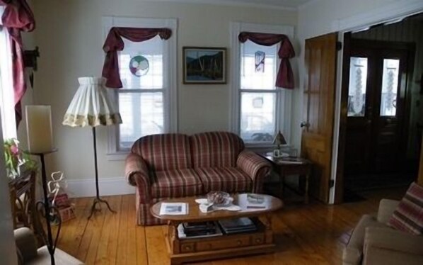 A living room with a striped sofa, a coffee table, and a lamp. There are two windows with curtains and a door. - The Colonel's In B&B (Fredericton)