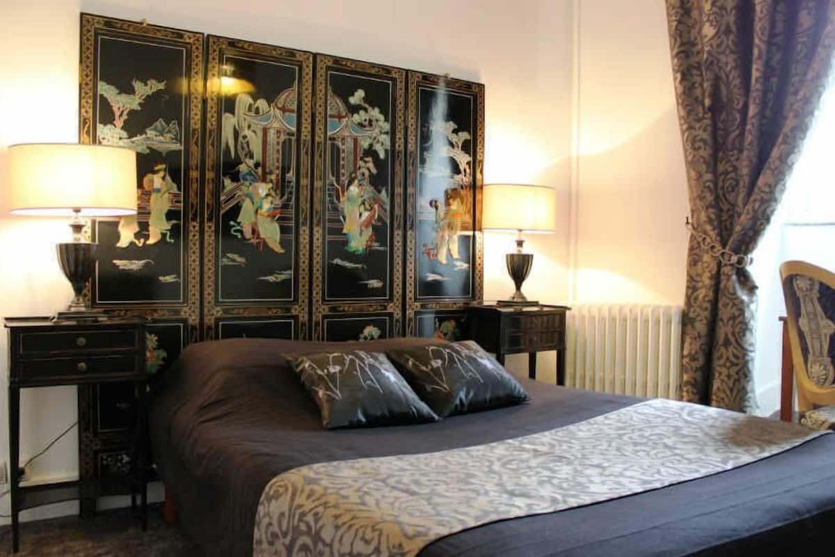 A hotel room with a large bed, two bedside tables with lamps, a decorative wall panel, and a radiator.