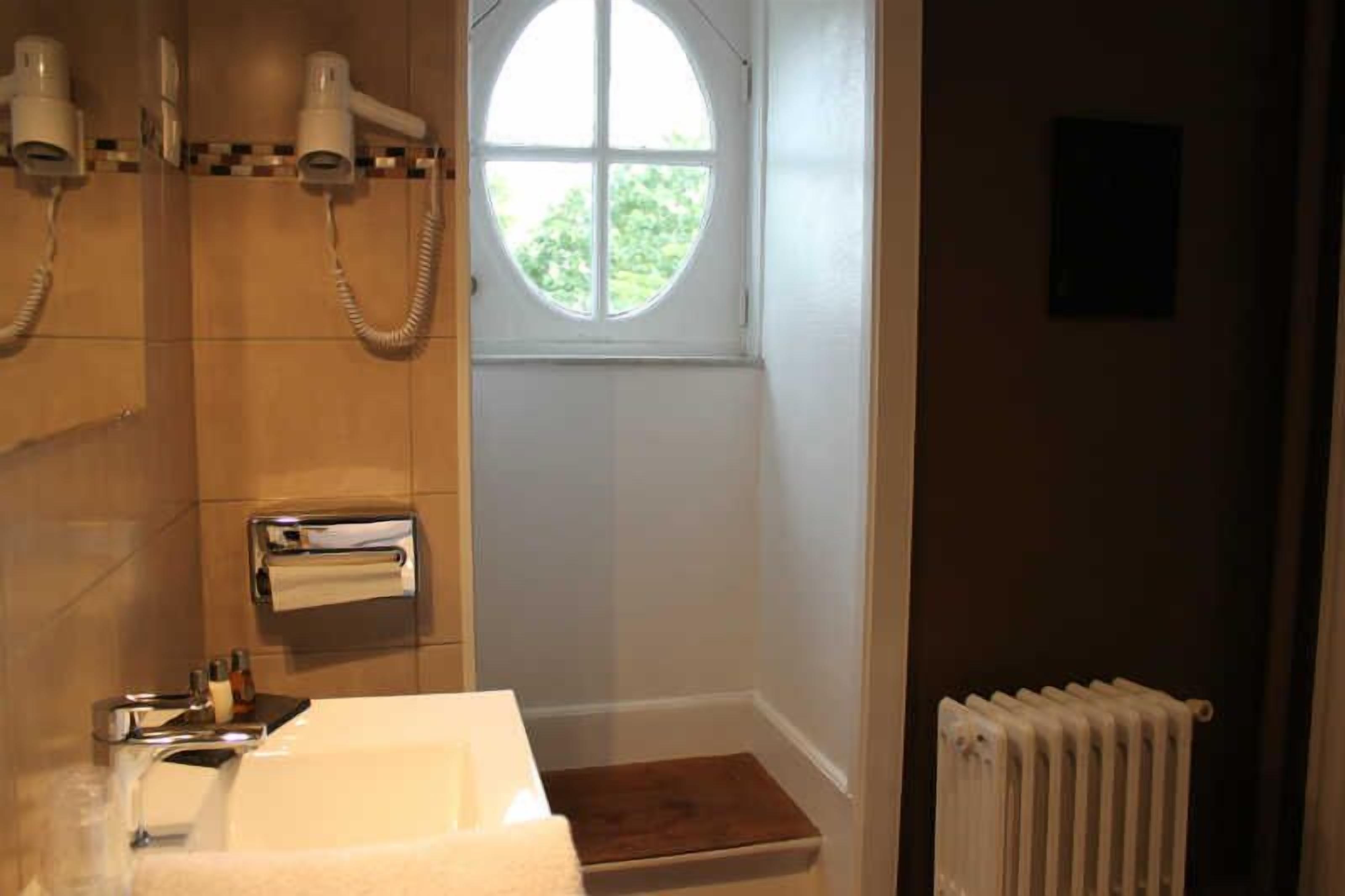 Un baño con lavamanos, dispensador de toallas, secador de pelo y ventana con vista a zonas verdes.