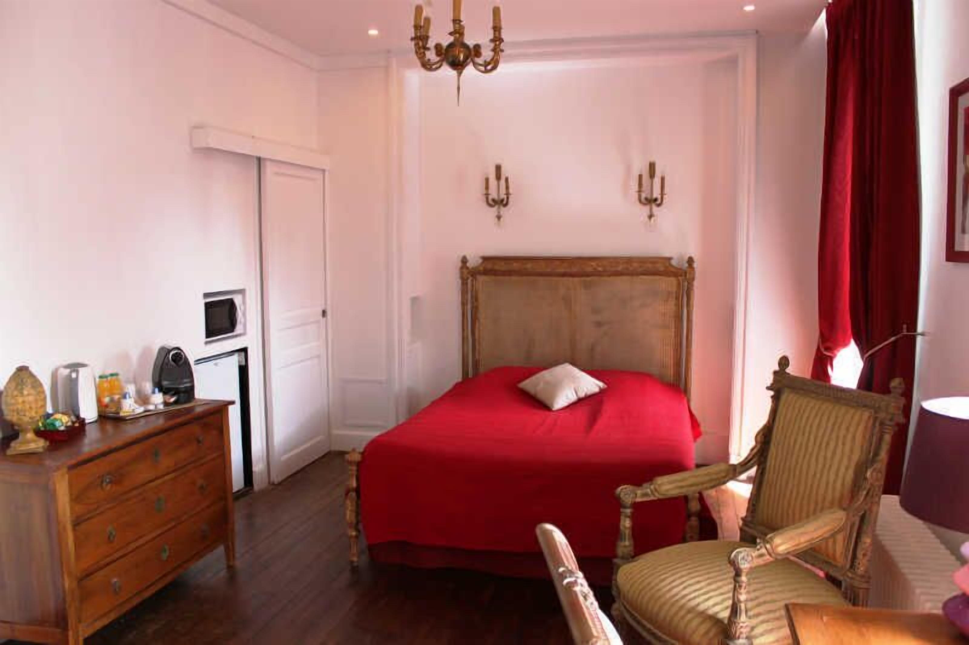 Un dormitorio con una cama de madera, un aparador, una silla, una lámpara y una cortina roja.
