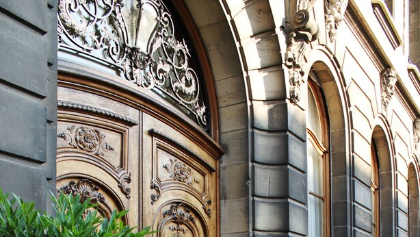Fachada de edificio con puertas de madera ornamentadas y pared de piedra.