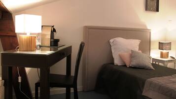 Un dormitorio con cama, mesita de noche, lámpara, silla y escritorio con lámpara.