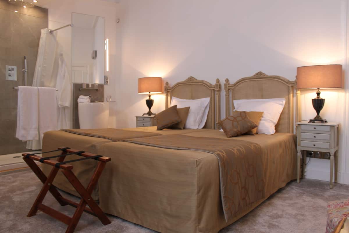 A neatly arranged bedroom with a large bed, two bedside tables, a wooden chair, and a shower area.