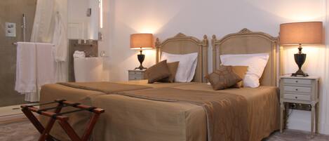 A neatly arranged bedroom with a large bed, two bedside tables, a wooden chair, and a shower area.